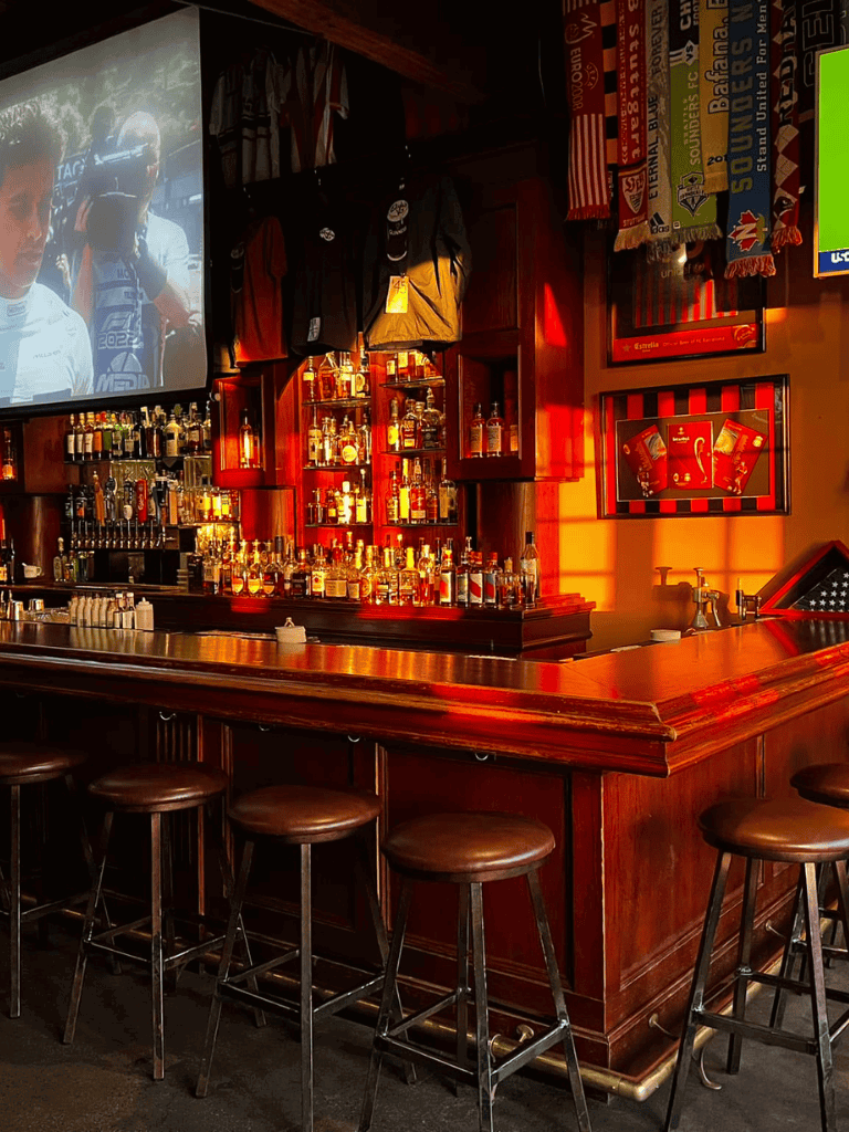 Cozy bar with liquor bottles and sports memorabilia, American bar ambiance, warm lighting, late-night entertainment.