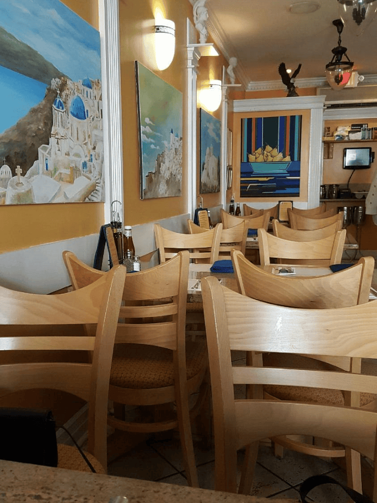 Colorful Greek-inspired restaurant interior with ocean-themed artwork and wooden chairs.