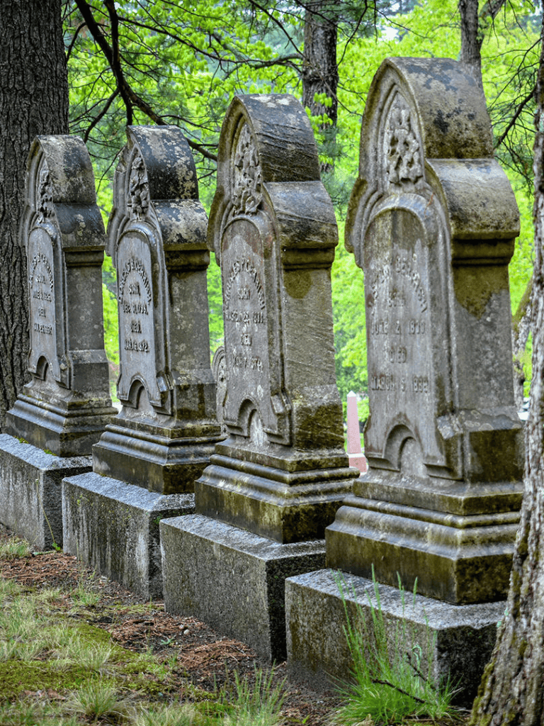 Ancient gravestones in a historic cemetery surrounded by lush green trees, showcasing memorial markers and historical significance.