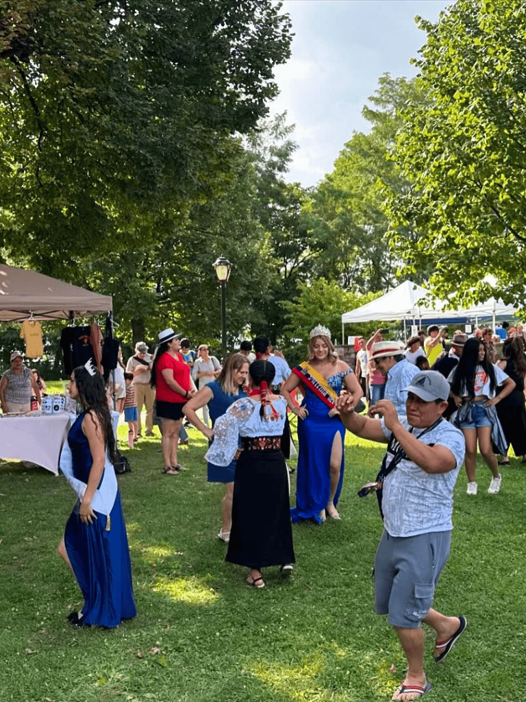 Colorful outdoor cultural festival with traditional costumes and dancing, lively crowd enjoying music and food under green trees.