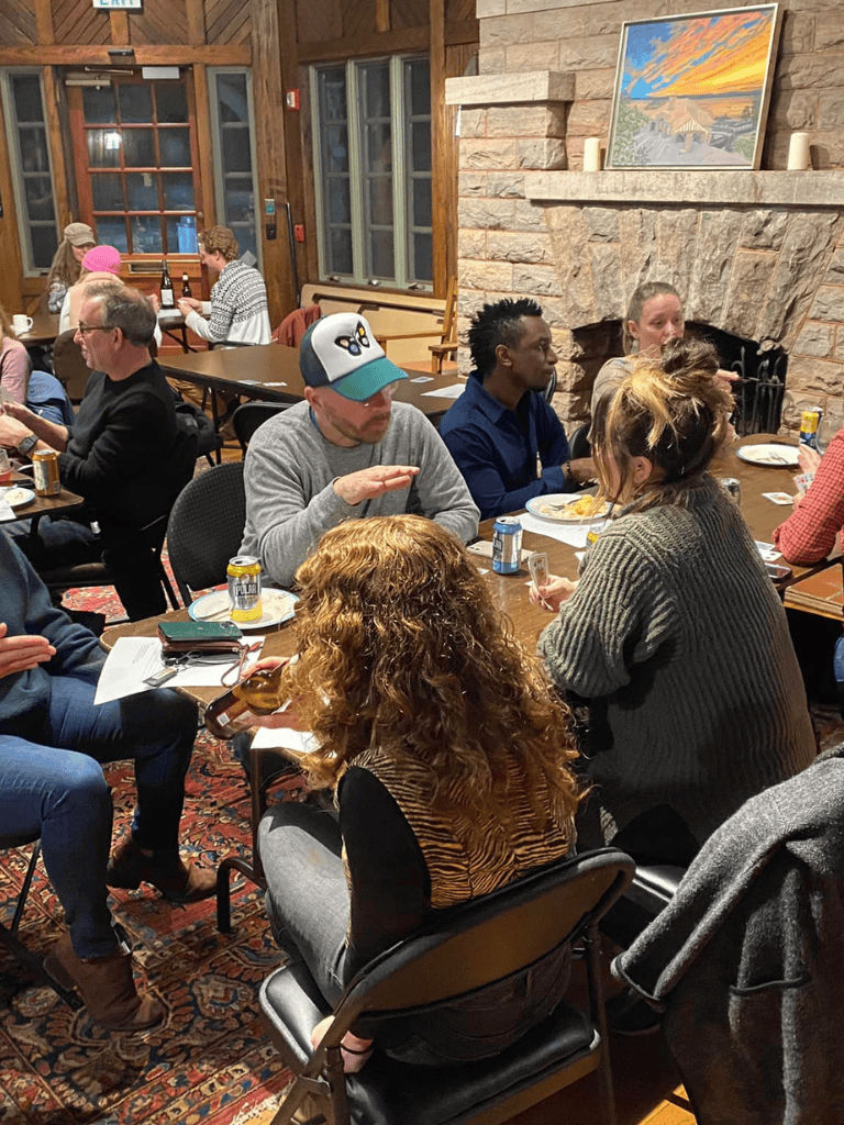 Cozy group dinner gathering in a rustic lodge with stone fireplace and warm lighting, emphasizing community and scenic ambiance.