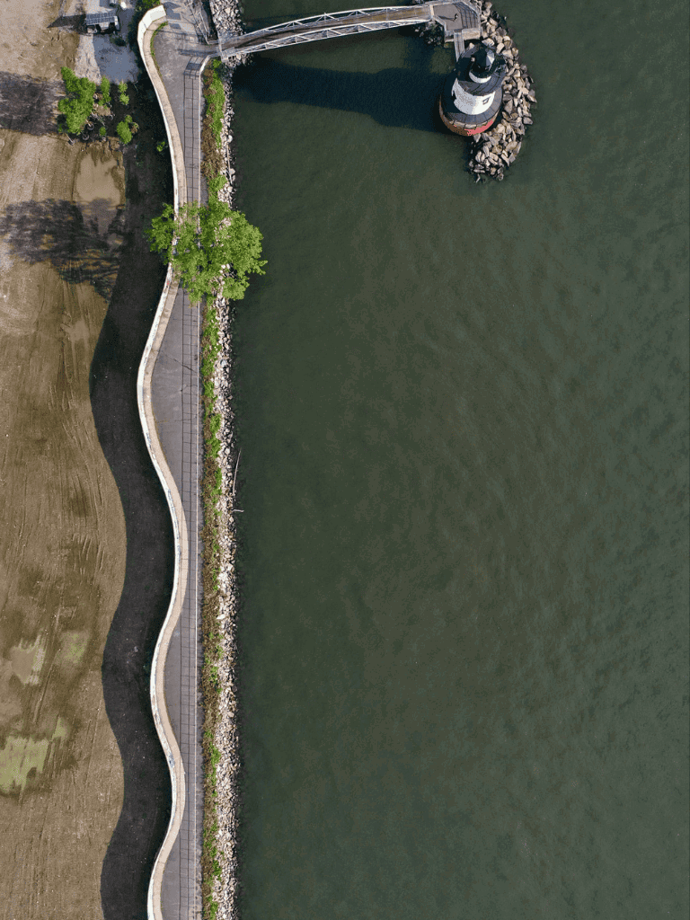 Seaside walkway with lighthouse and rocky shoreline, scenic waterfront and walking trail.