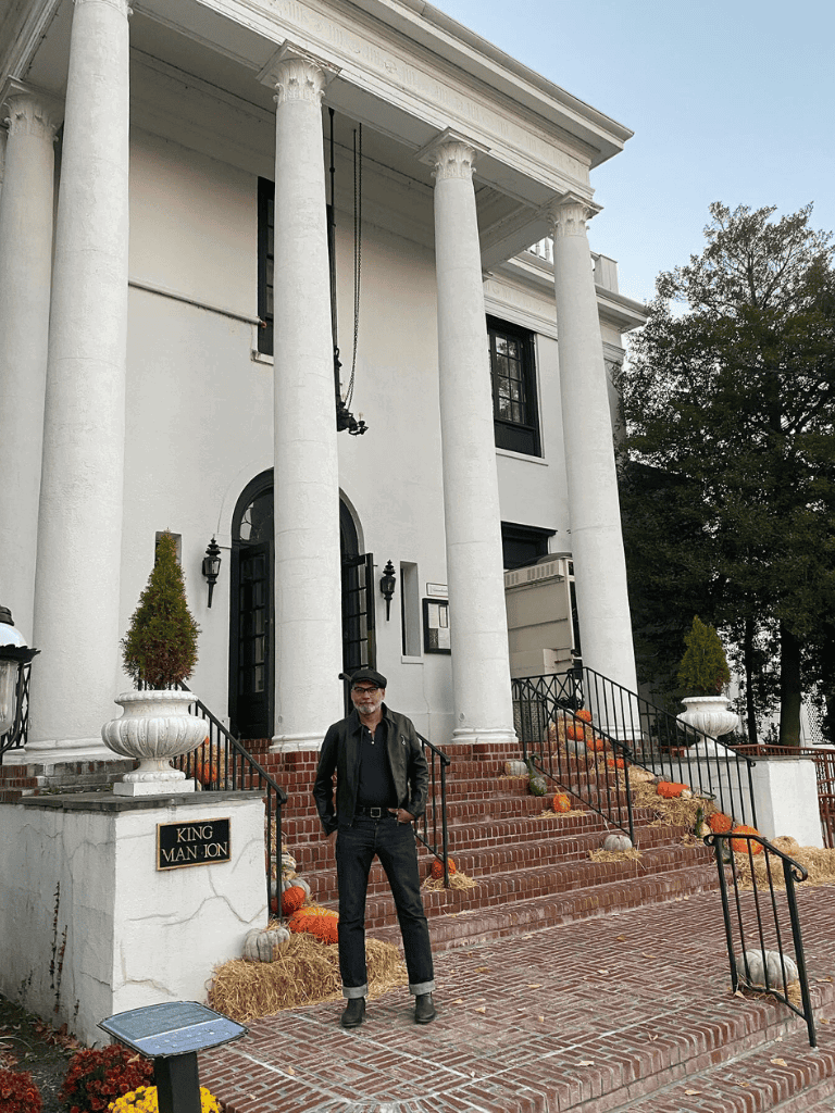 Elegant white historical mansion with tall columns, fall decor, and a person standing on brick stairs.