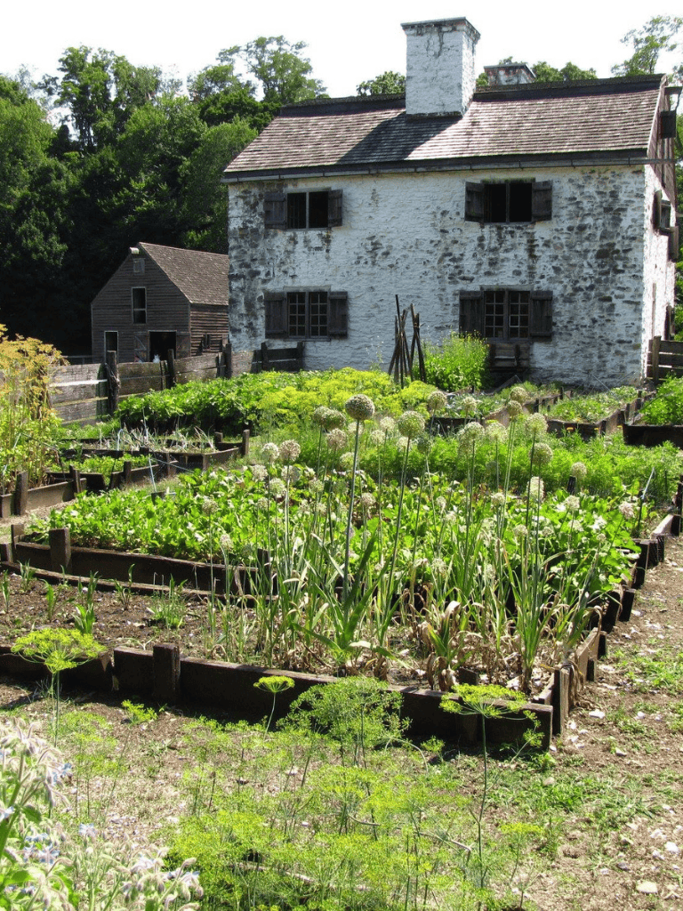 Rustic farmhouse with lush vegetable garden, scenic wooded backdrop, and historic charm for garden enthusiasts.