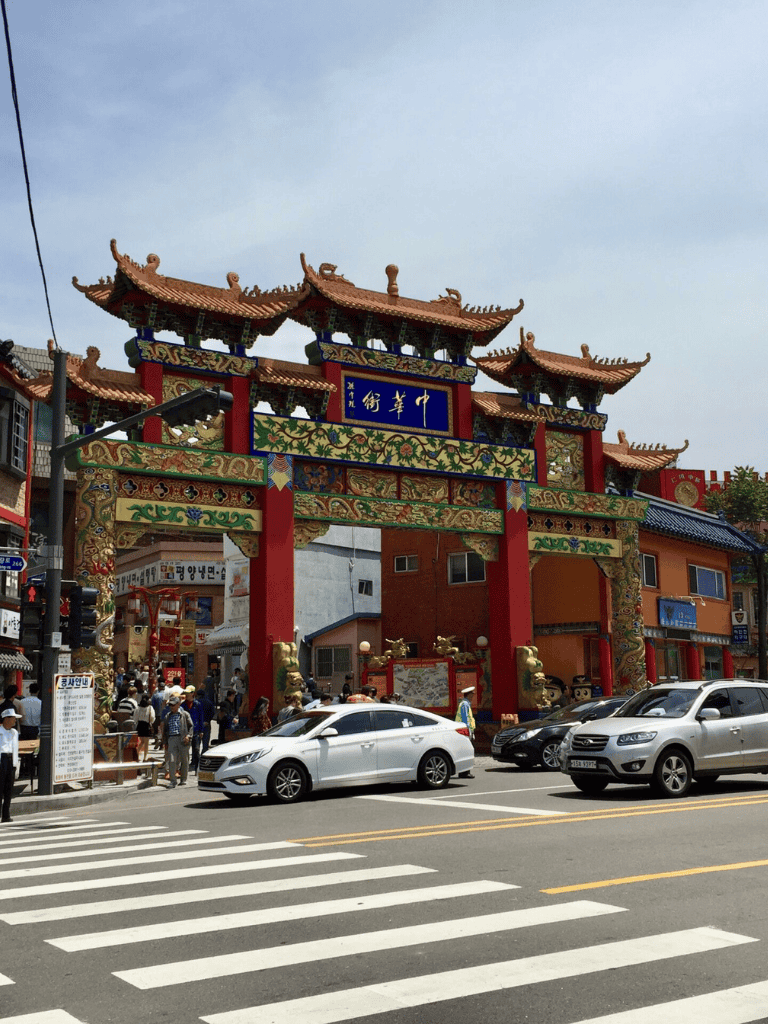 Colorful traditional Chinese gate in Chinatown with cars and pedestrians.
