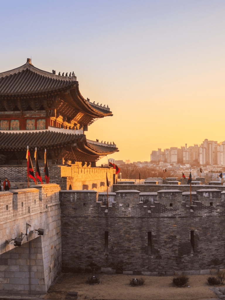 Ancient fortress with traditional Korean architecture at sunset, historic city landmarks nearby.