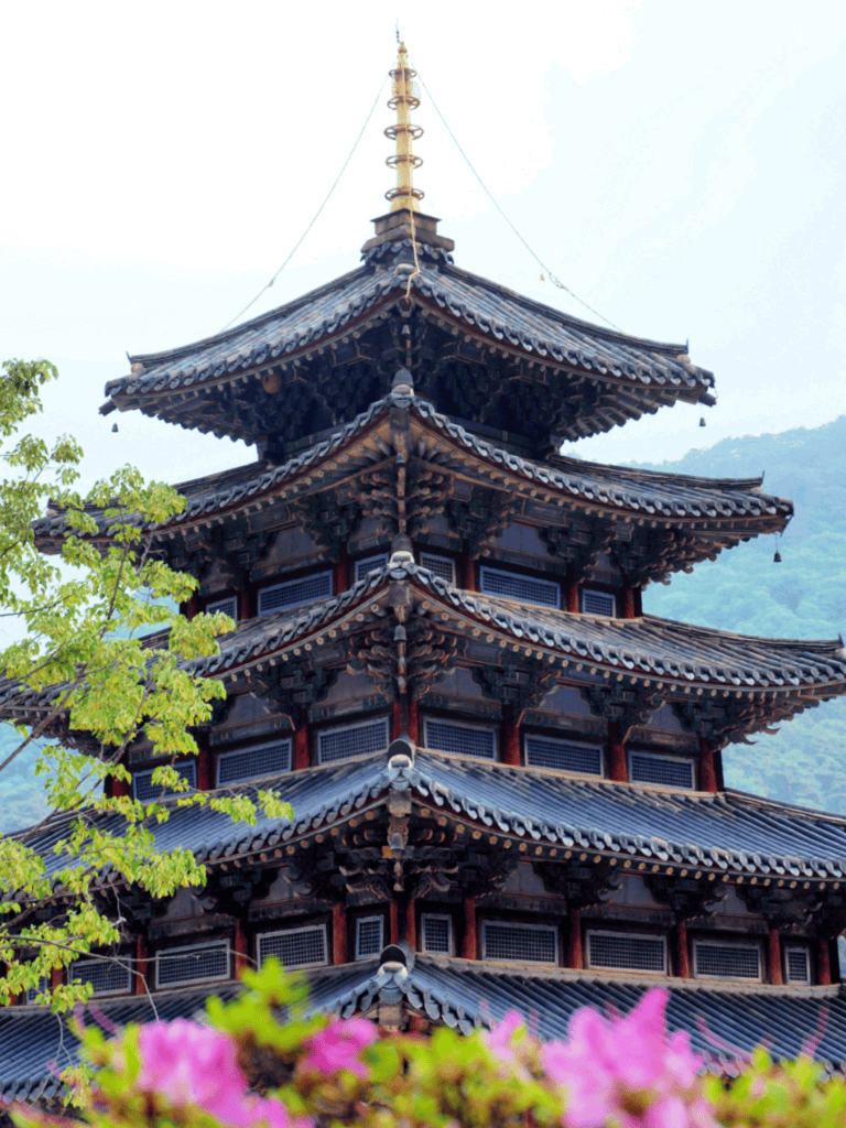 Ancient East Asian temple pagoda with layered roofs and intricate woodwork, surrounded by lush greenery.