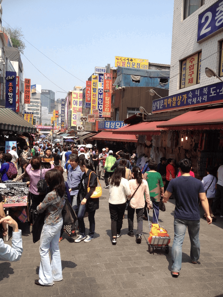 Bustling street market in Seoul, South Korea with shoppers and colorful signs.