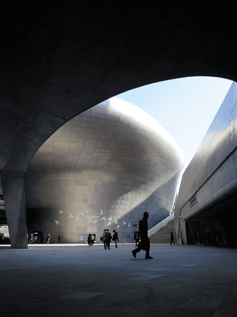 Modern architectural building with metallic curves and people walking around in an urban setting.