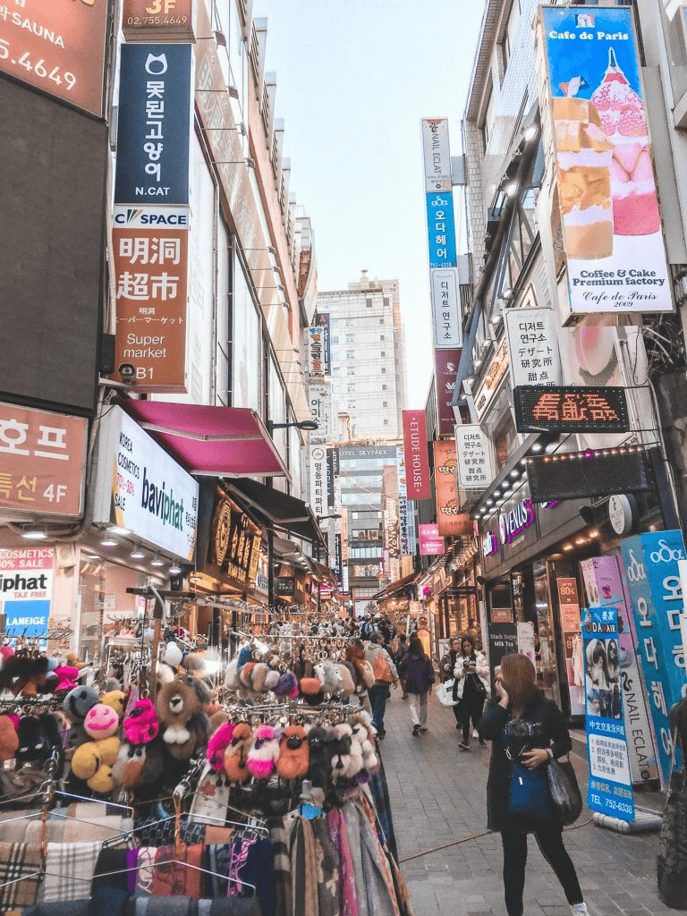 Vibrant street in Seoul with shops, colorful accessories, and busy shoppers in a bustling urban setting.