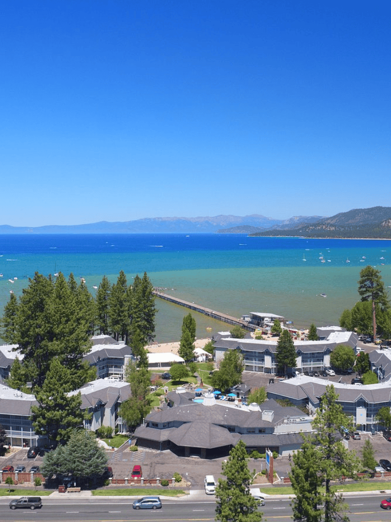 Tranquil lakeside resort with mountains, boats, and lush greenery in a scenic coastal setting.