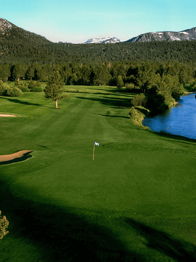 Lush golf course with mountain backdrop and river, perfect for outdoor recreation and scenic views.