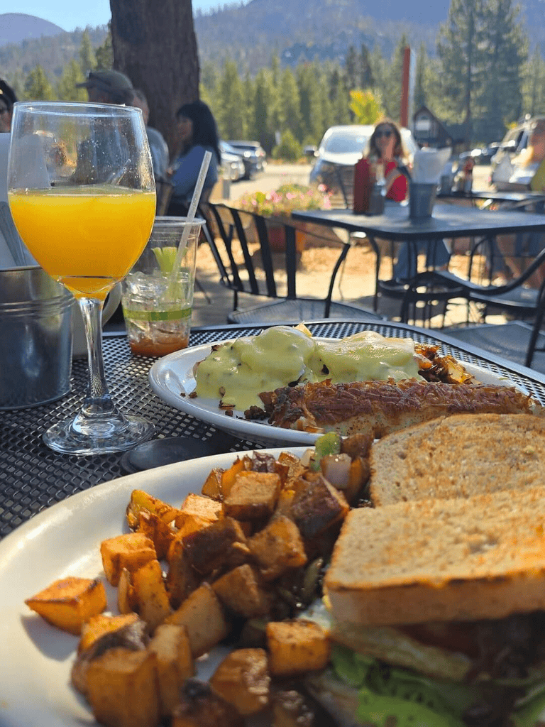 Juicy breakfast with roasted potatoes, eggs benedict, and fresh orange juice in mountain outdoor restaurant.
