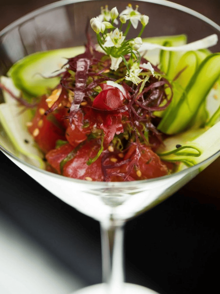 Fresh garden salad with mixed greens, edible flowers, and cucumber slices in a martini glass.
