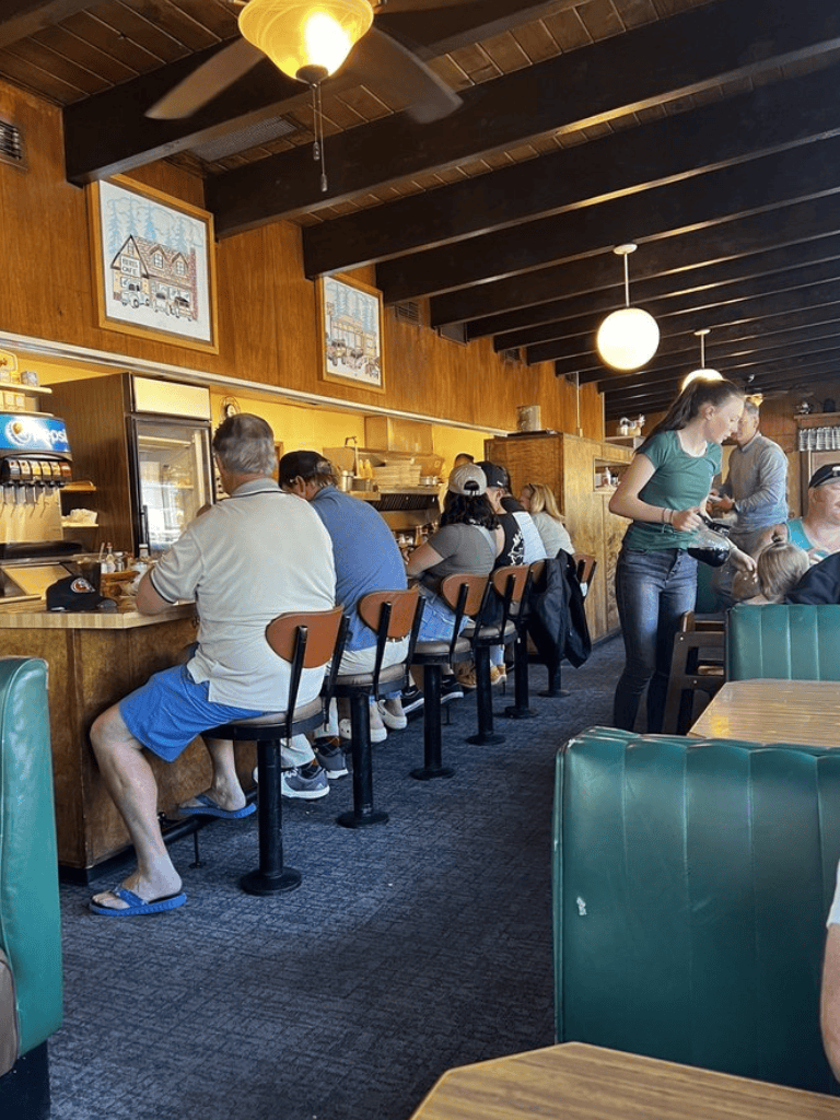 Busy diner at QuestForDirections restaurant, with customers seated at the counter and servers taking orders.