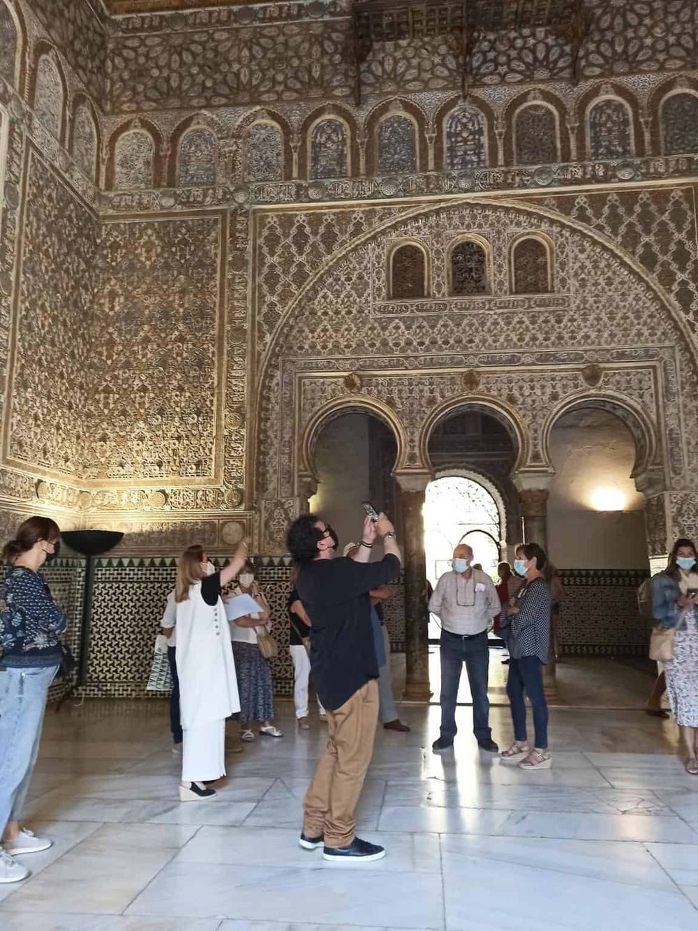 Intricate Islamic architectural interior with tourists exploring and taking photos at a historical site.