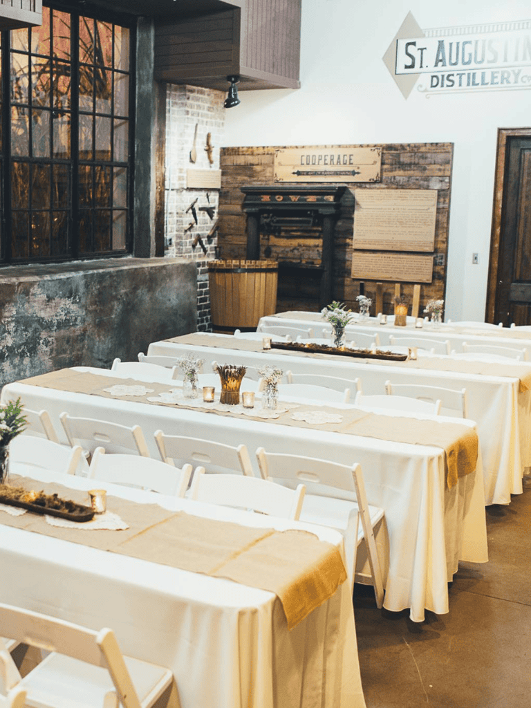 Cozy rustic wedding reception setup with long tables, white linens, floral centerpieces, and vintage decor.