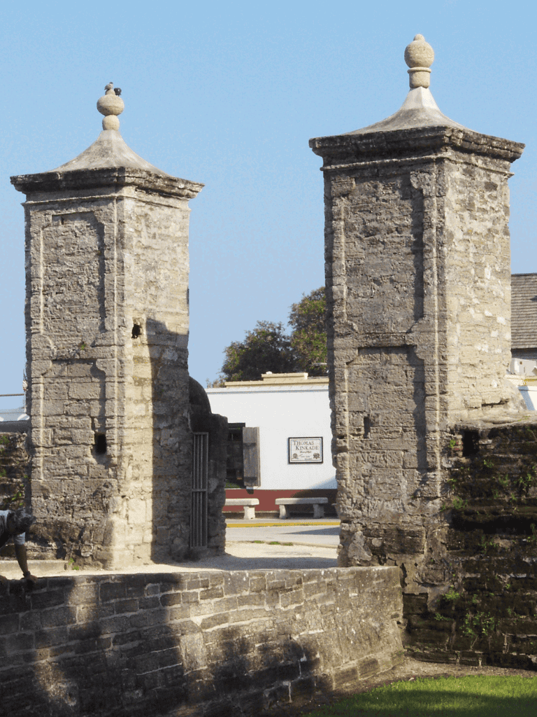 Stone historic gate with two towers and decorative finials at the top, in a sunny setting.