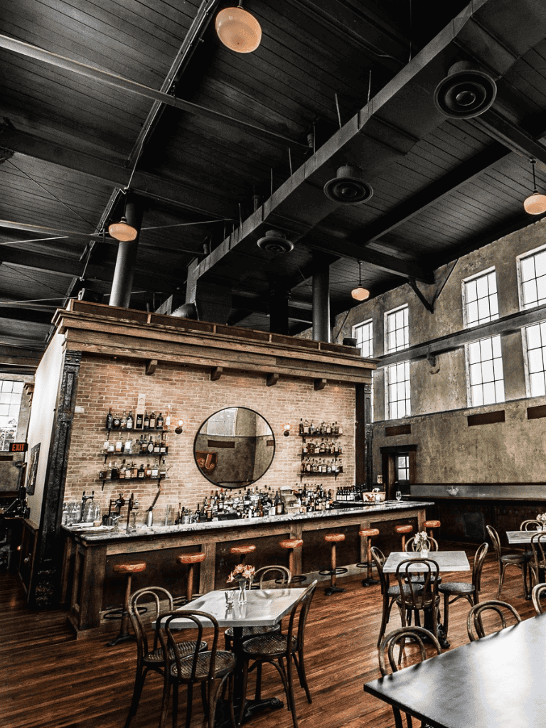 Cozy industrial-style bar with exposed brick, wood accents, high ceilings, and vintage decor for a welcoming atmosphere.
