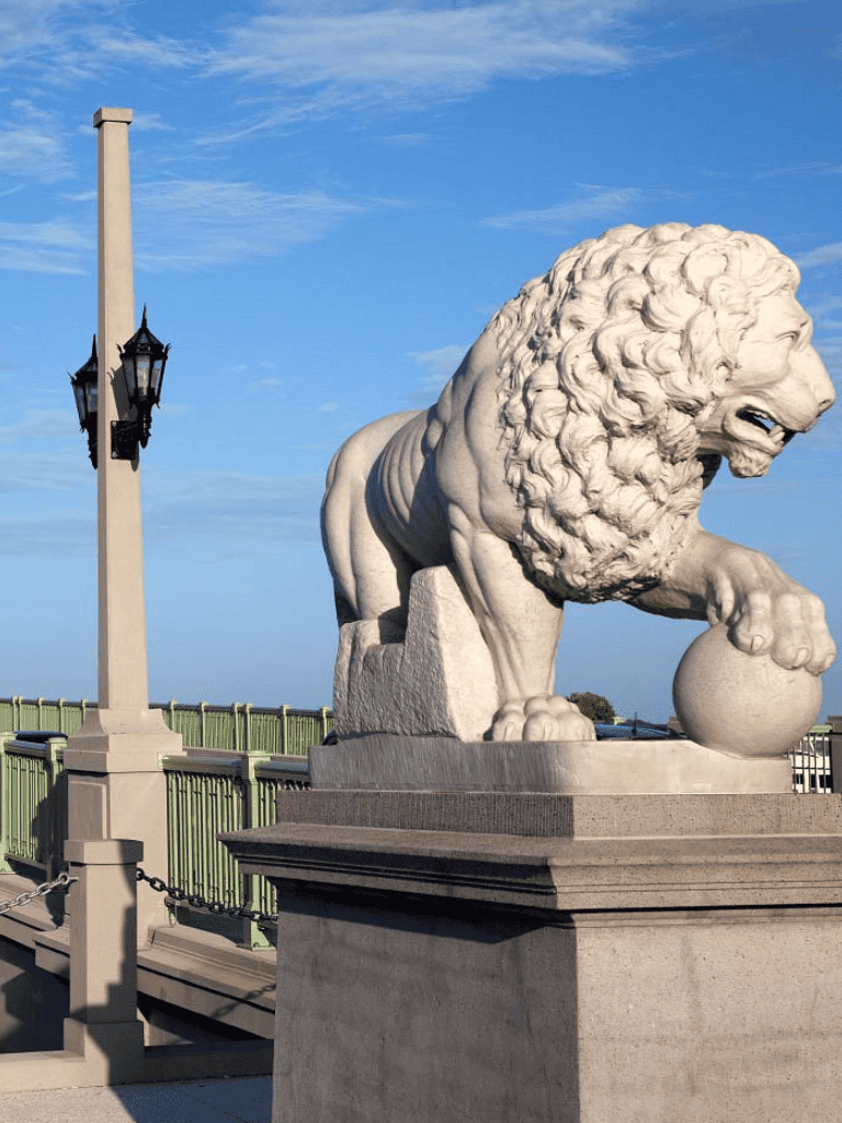 Majestic lion statue on a city bridge, symbolizes strength and courage, with a clear blue sky background.