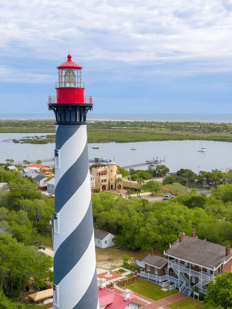 Colorful lighthouse with coastal scenery and sailing boats in the background.