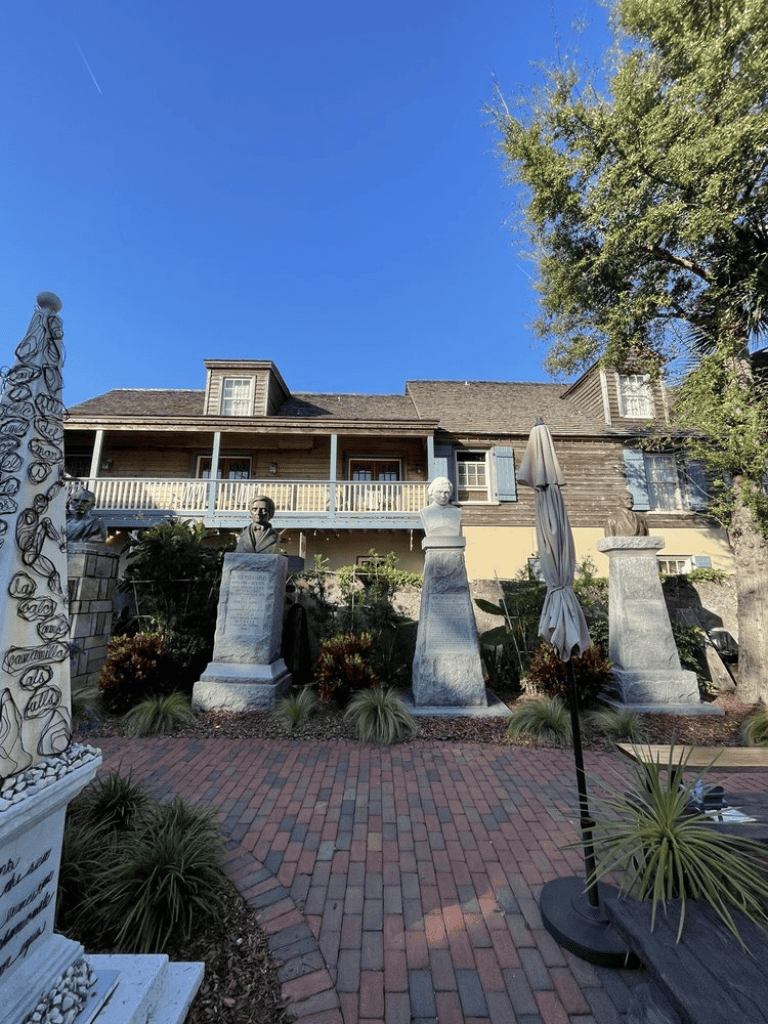 Vintage house with bust sculptures and brick pathway under clear blue sky.