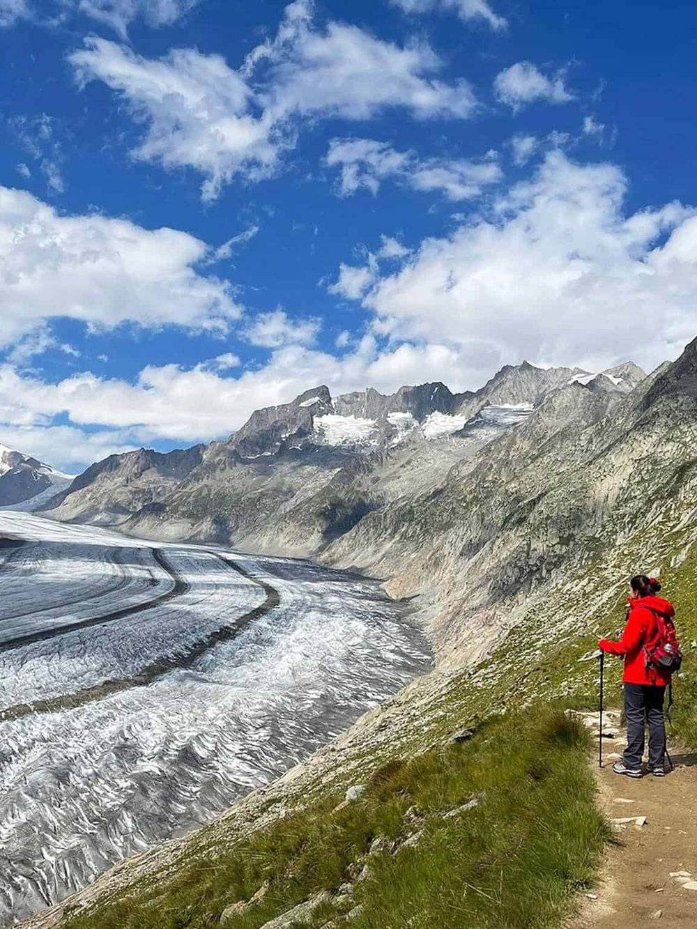 Vibrant mountain landscape with hiking trail, glaciers, and a hiker enjoying scenic views in nature.