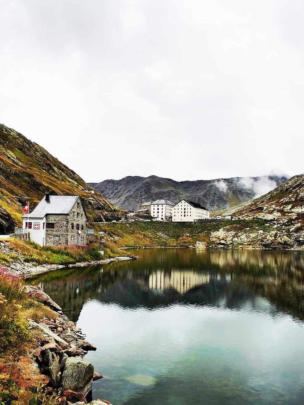 Serene mountain landscape with lake, historic buildings, and cloudy sky, perfect for travel exploration.