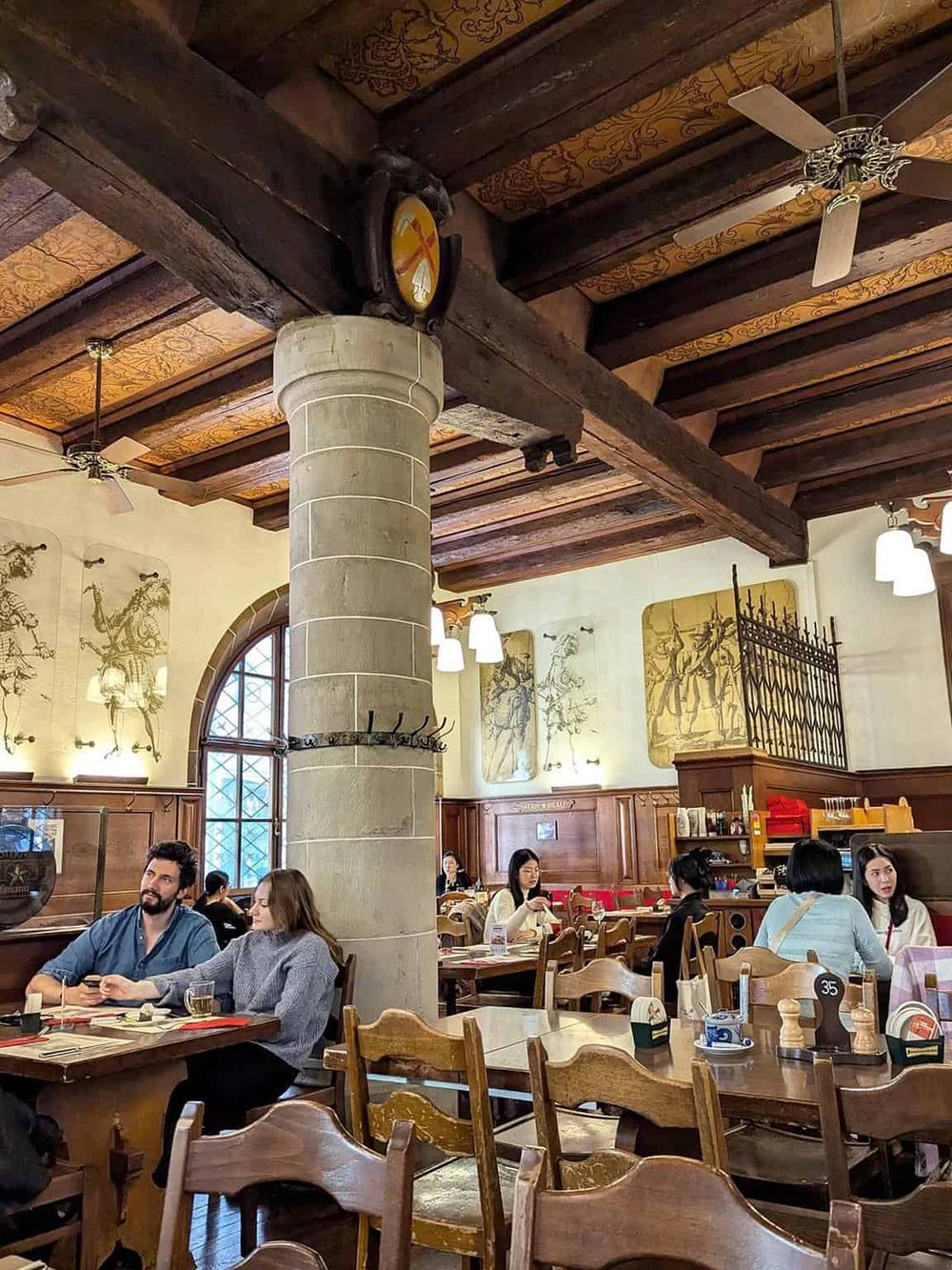 Cozy restaurant interior with wooden beams, vintage artwork, and diverse guests enjoying meals.