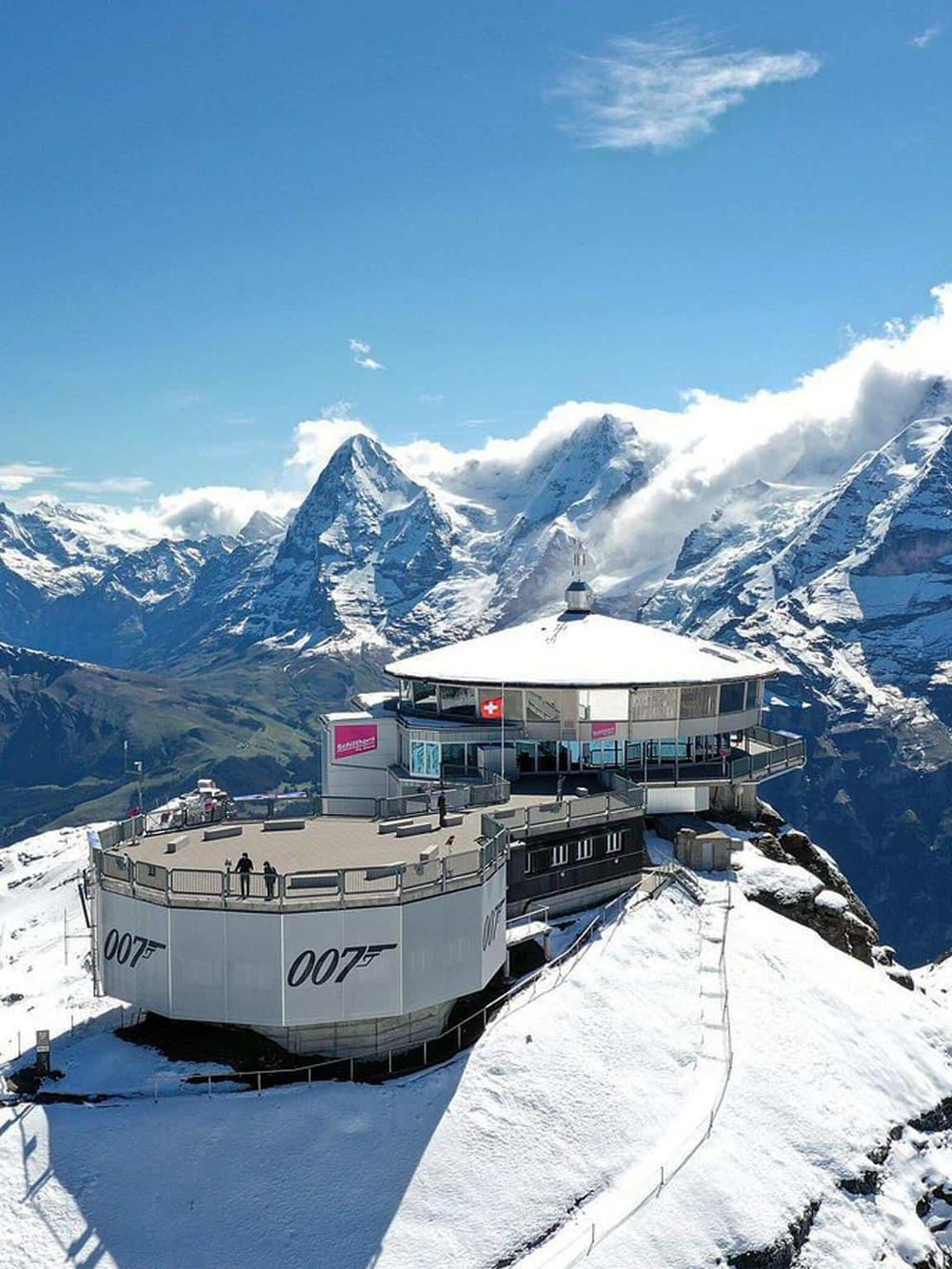 Panoramic view of the Swiss mountains with a modern observation deck and the James Bond Mountain logo in the foreground.