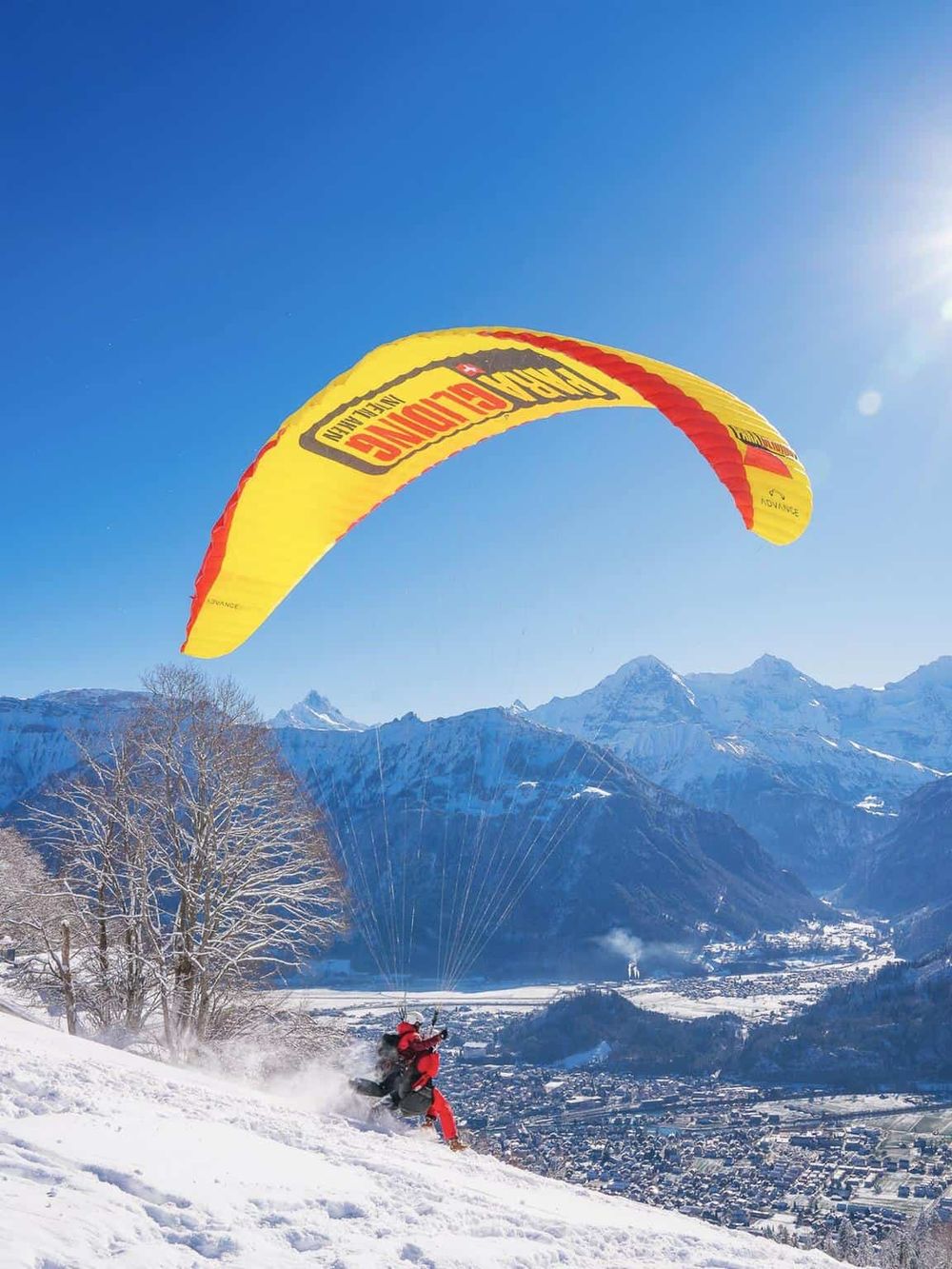 Colorful paragliding in snowy mountain landscape with clear blue sky.