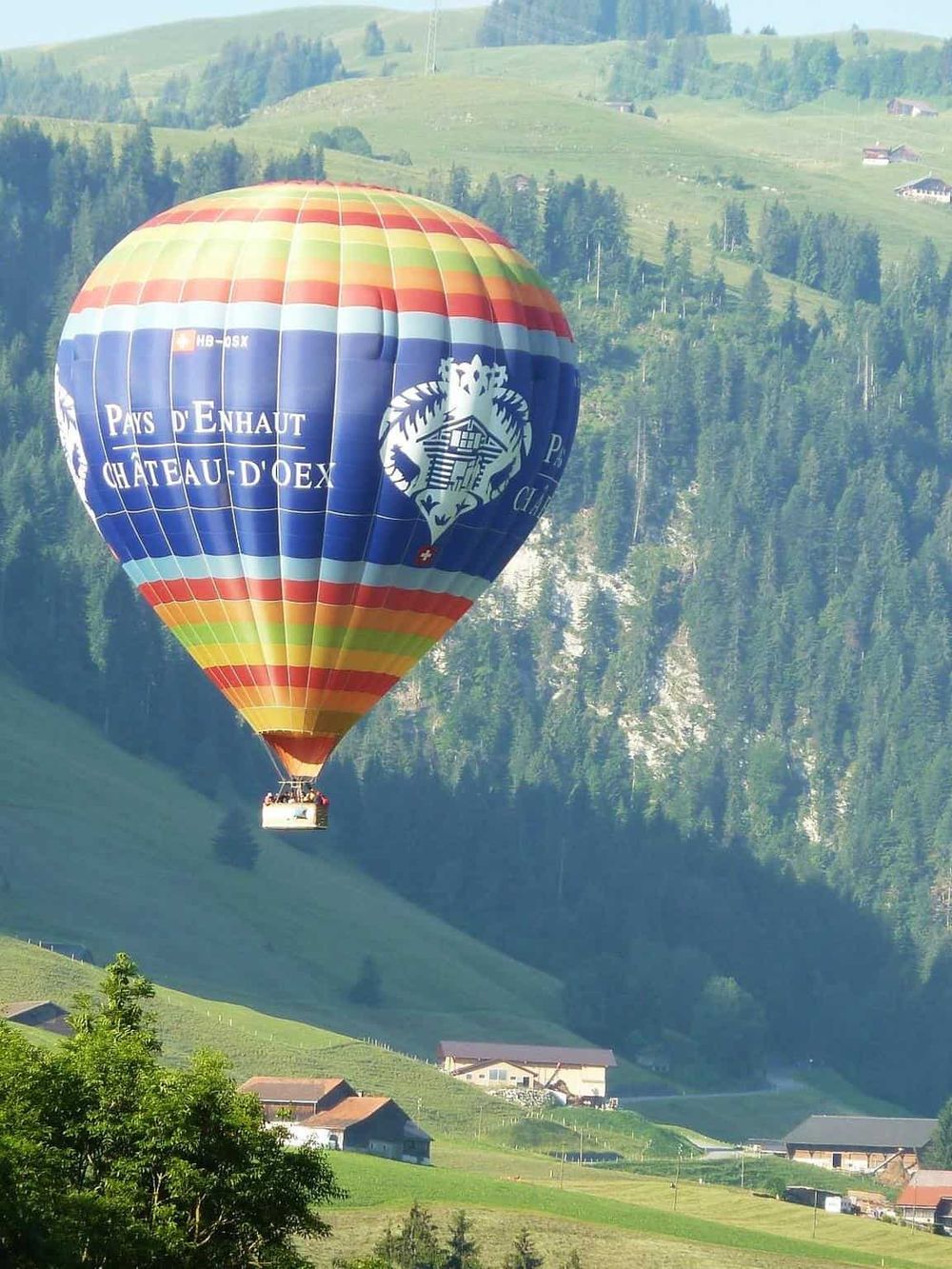 Colorful hot air balloon flying over green hills and mountains in the countryside.