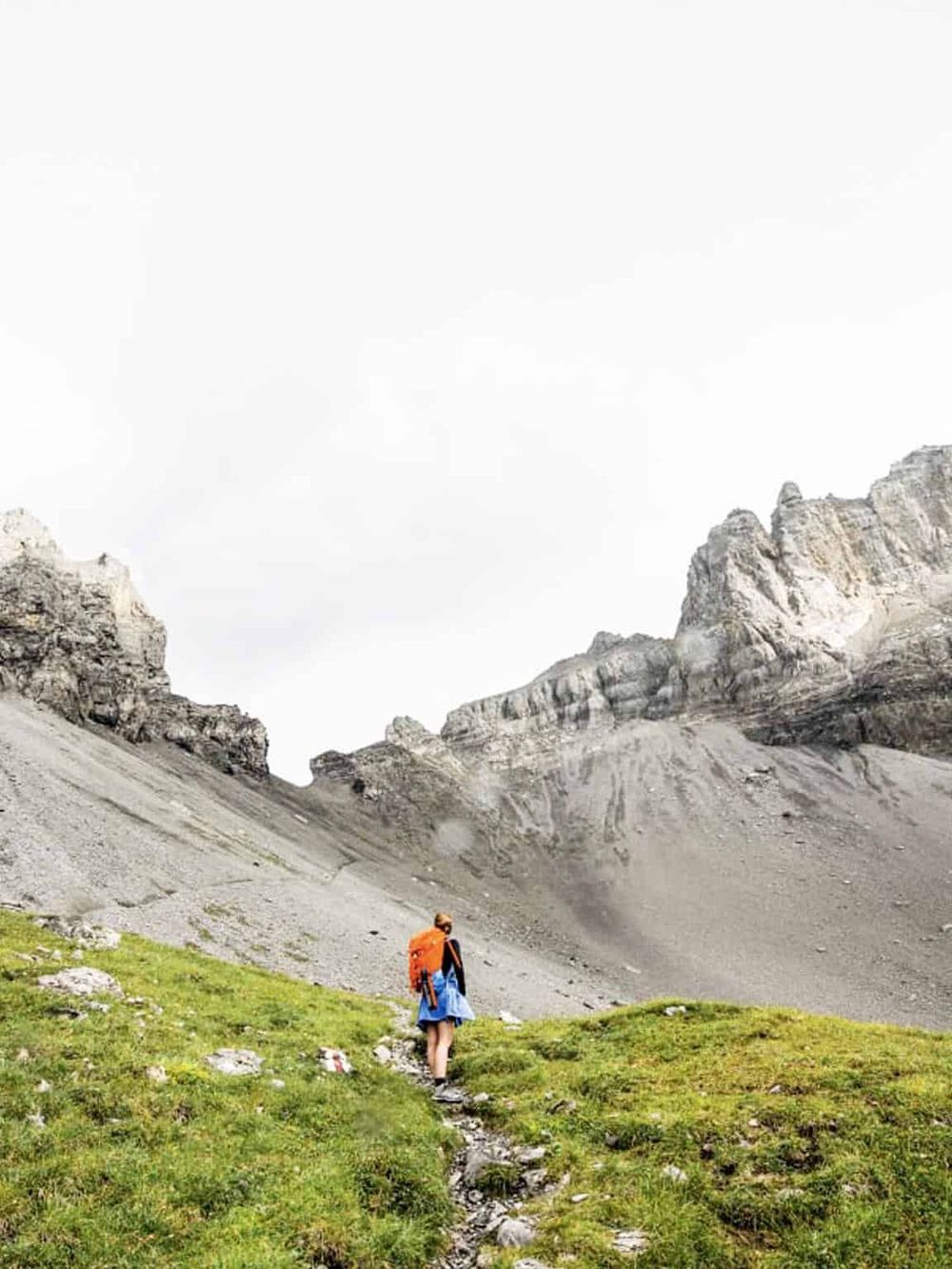 Hiker trekking on mountain trail with rocky peaks, adventure, and outdoor exploration.