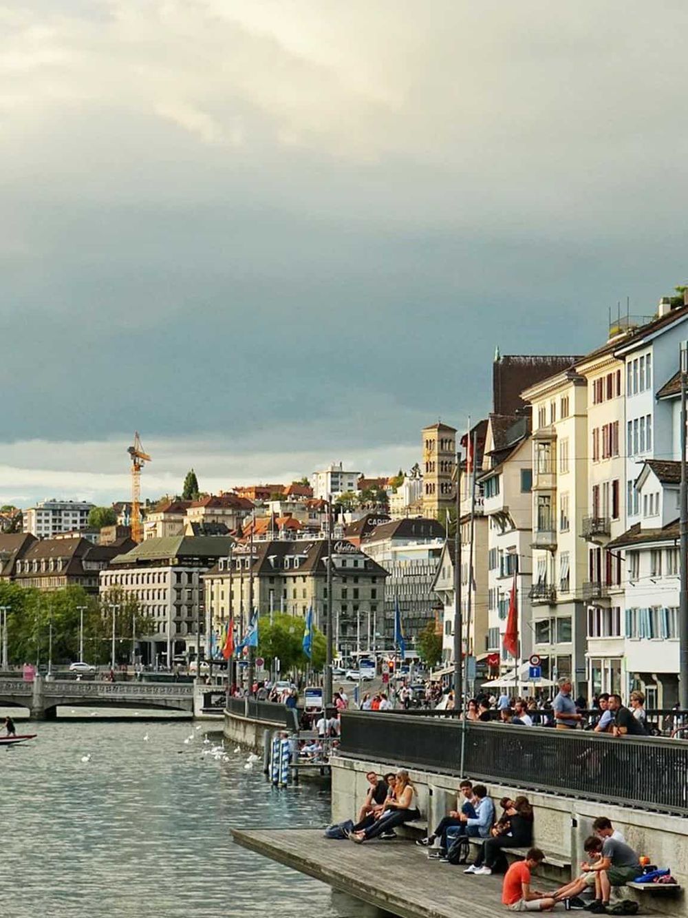 Scenic Zurich lakeside view with historic buildings, people relaxing, and city skyline, perfect for exploring Swiss travel destinations.