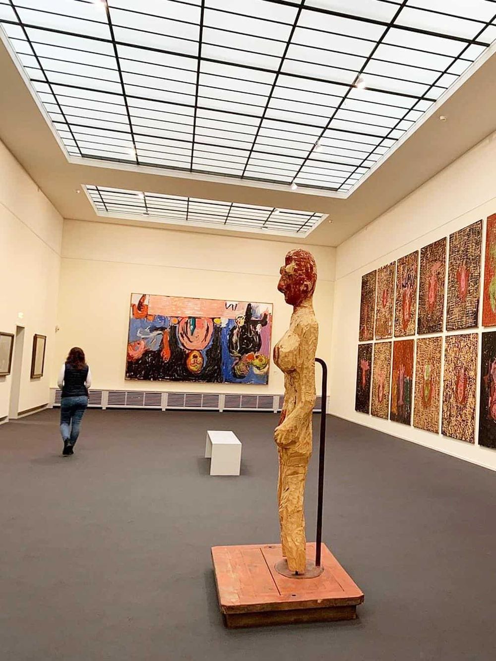 Vivid sculpture of a human figure displayed in an art gallery with colorful paintings on the walls.