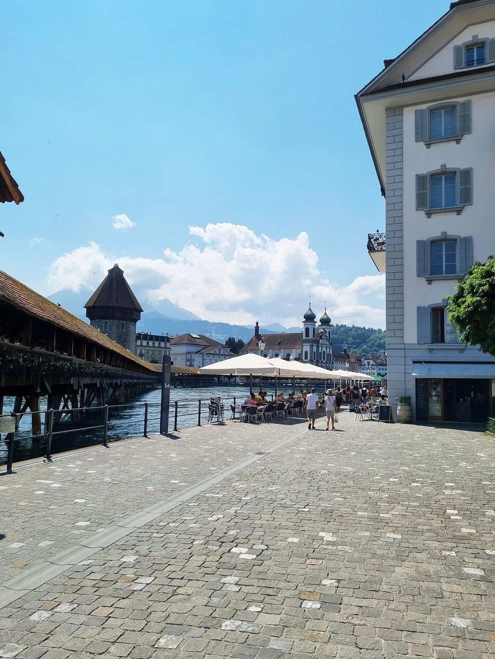 Scenic lakeside promenade with outdoor cafes, historic architecture, and mountain views in Switzerland.