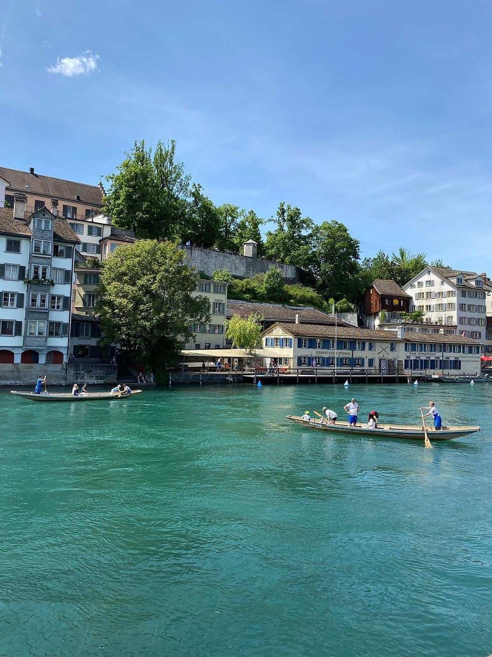 Colorful lakeside Swiss village with boats on turquoise water and lush green hills.