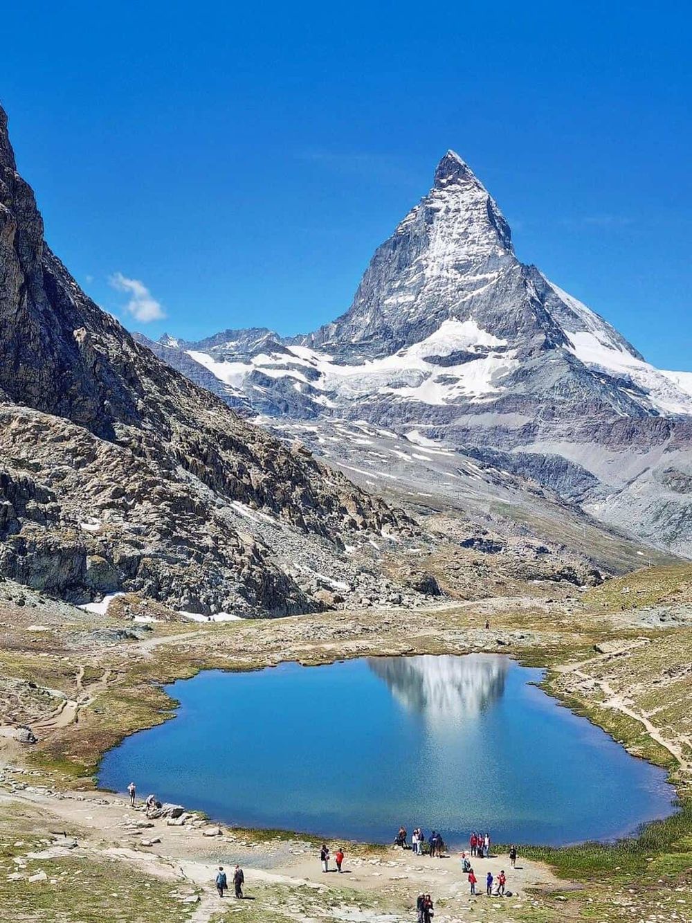 Stunning mountain landscape featuring the iconic Matterhorn, alpine lake, and hikers enjoying the scenic views in the Swiss Alps.