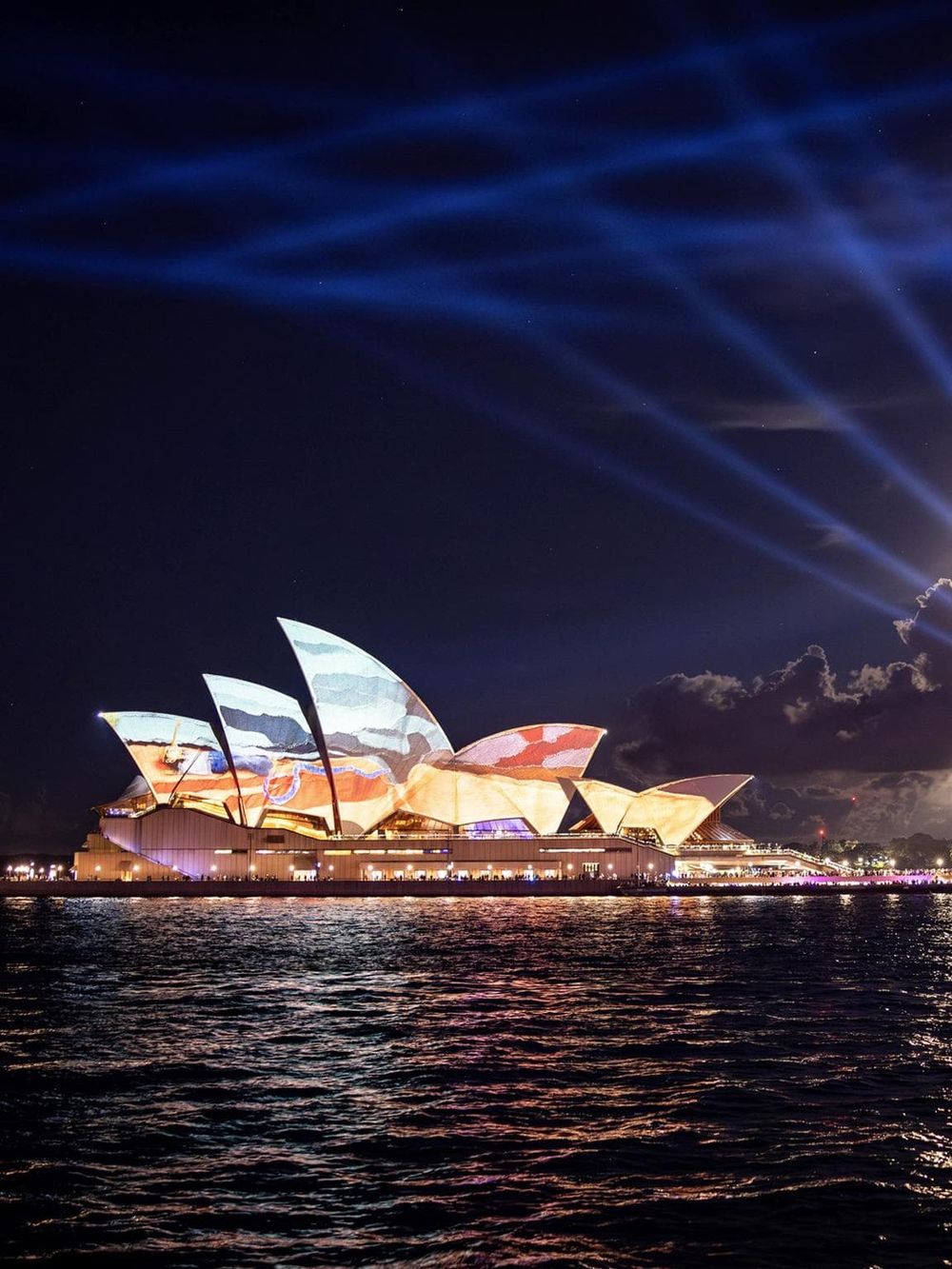 Light show at Sydney Opera House, Australia, with dynamic projections and vibrant water reflections.