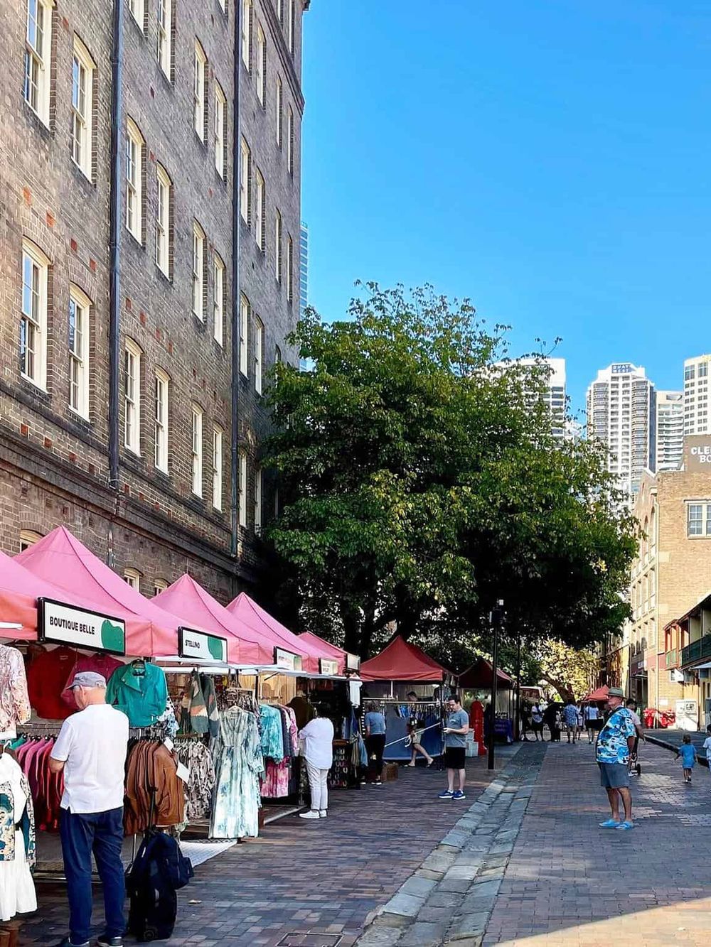 Vibrant outdoor market under pink tents on a city sidewalk with historic brick buildings and modern skyscrapers.