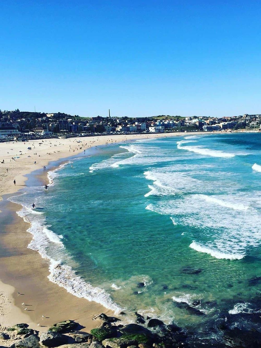 Bright sunny beach with clear blue waters and cityscape in the background, perfect for vacation and relaxation.