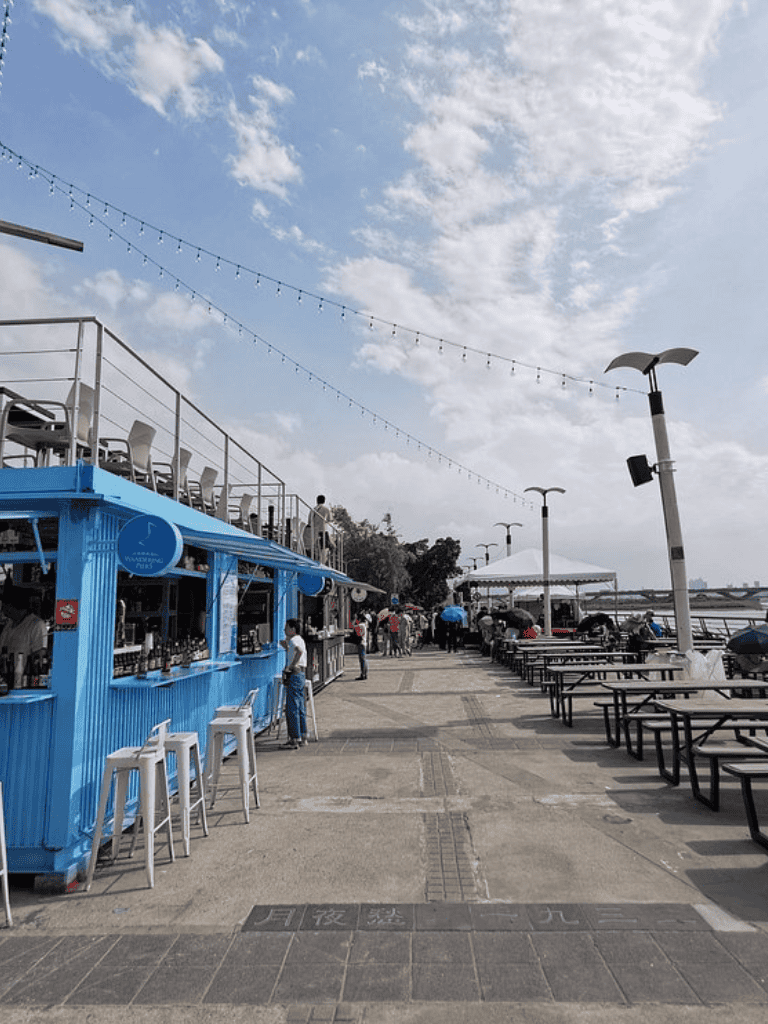 Blue seaside bar and restaurant with outdoor seating, string lights, and view of the dock and sky, perfect for beachside dining.