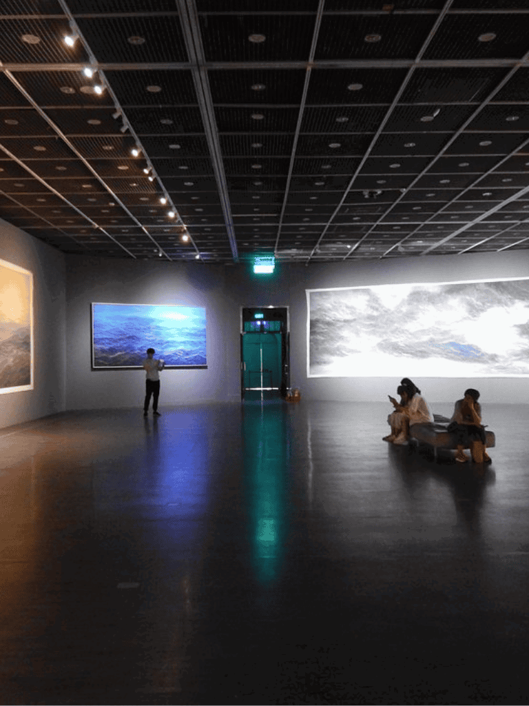 Vivid art gallery with large landscape paintings and visitors viewing artwork in a modern exhibition space.