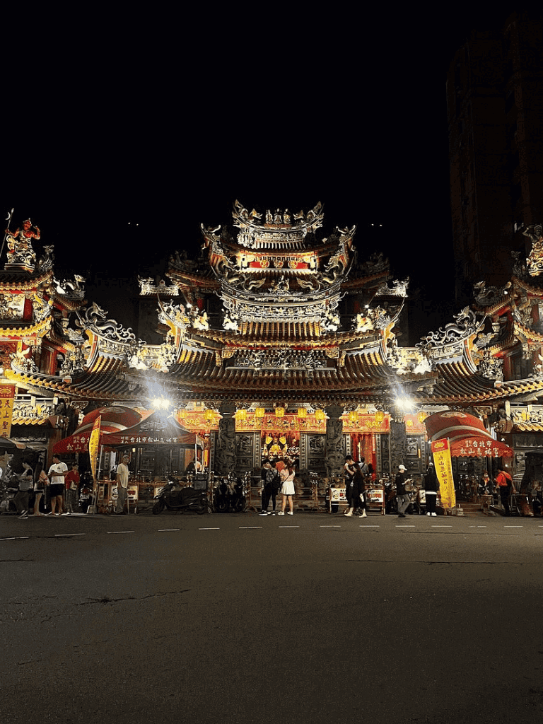 Intricate traditional Chinese temple lit up at night with visitors and vibrant decorations.