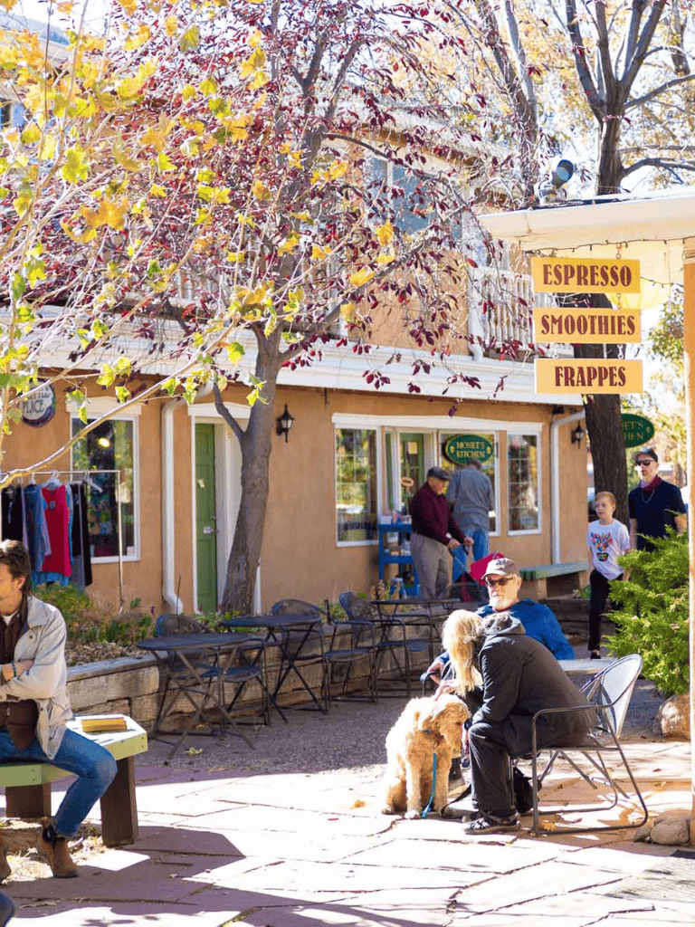 Outdoor coffee shop with fall foliage, serving espresso, smoothies, and frappes, surrounded by customers and pets.