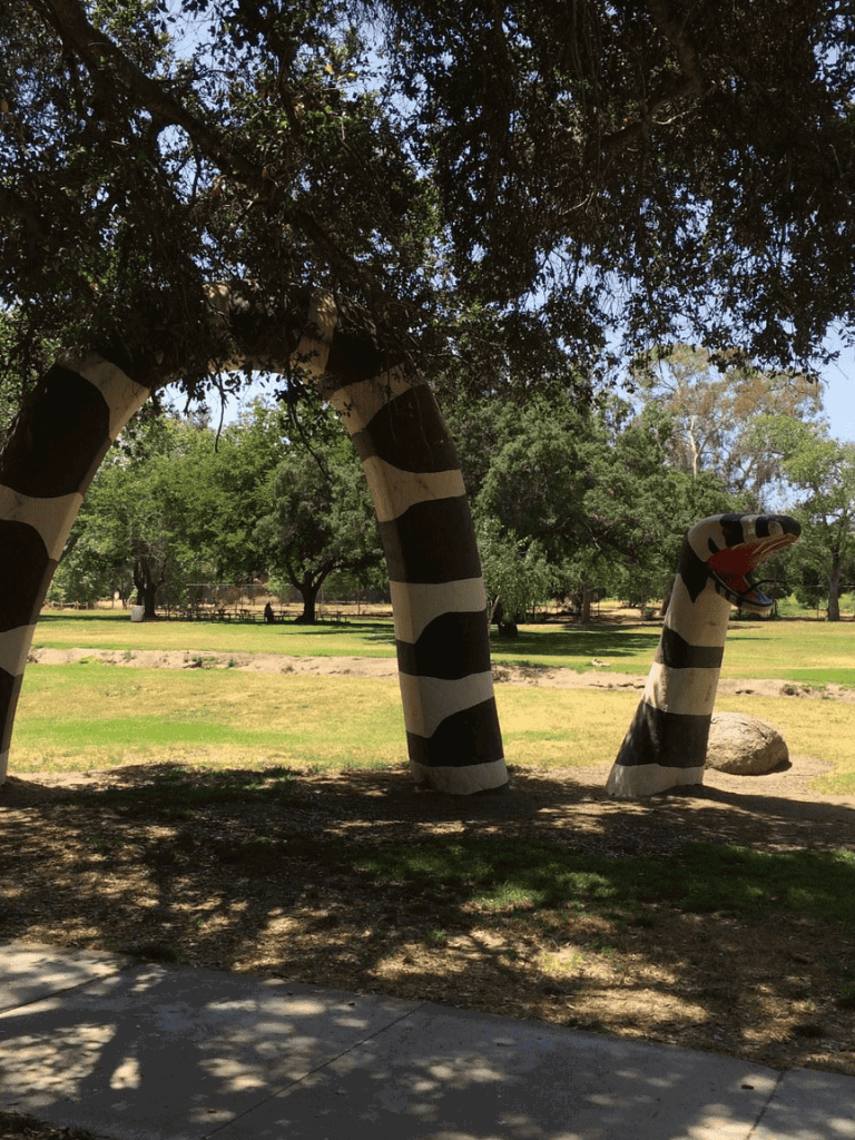 Colorful striped snake sculpture in park surrounded by trees and greenery.