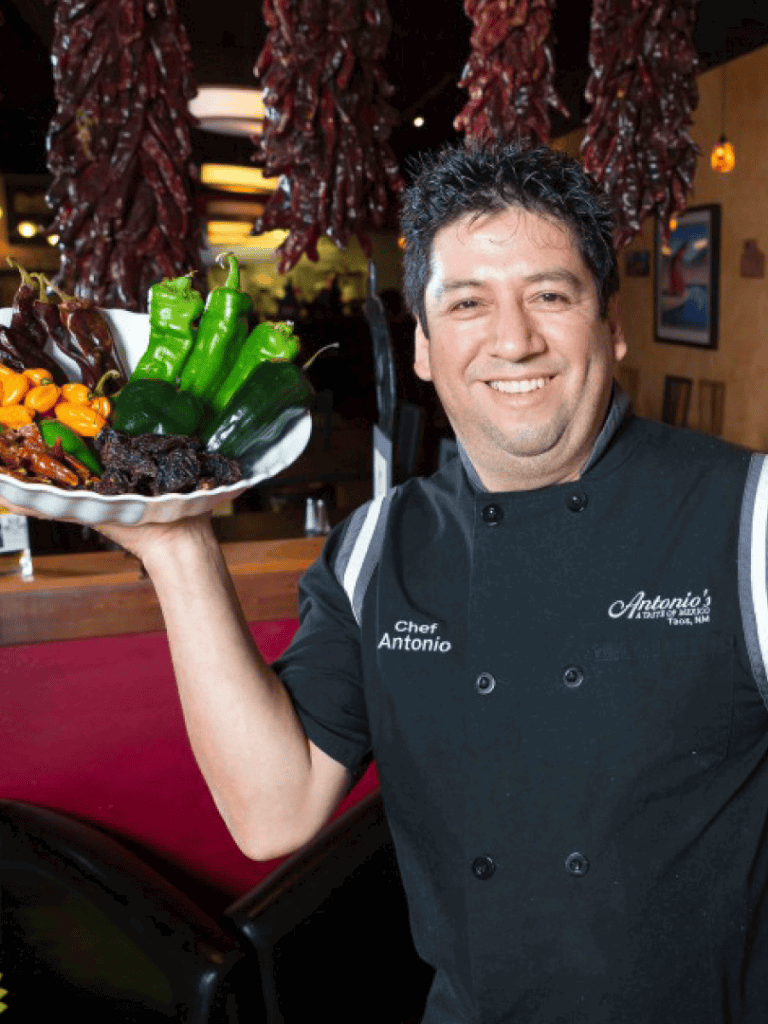 Vibrant chili peppers and authentic Mexican dishes held by Chef Antonio at a festive restaurant.