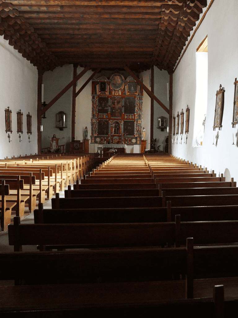 Quiet church interior with wooden pews, religious artwork, and altar in a historic setting.