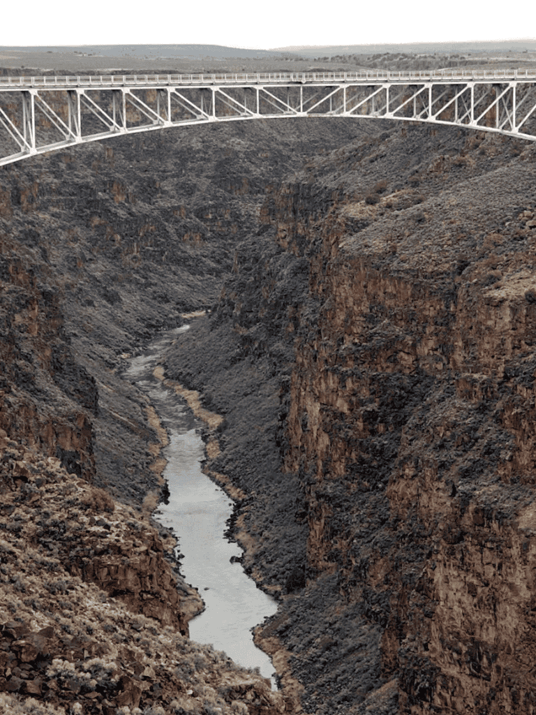 Wide canyon with bridge spanning over deep river gorge and rugged cliffs.