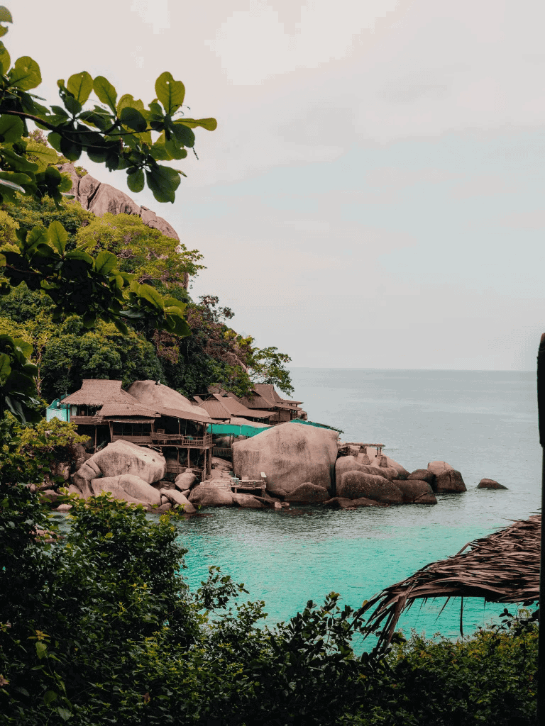 Bungalow resort on rocky coastline with lush greenery and turquoise sea, tropical island getaway.